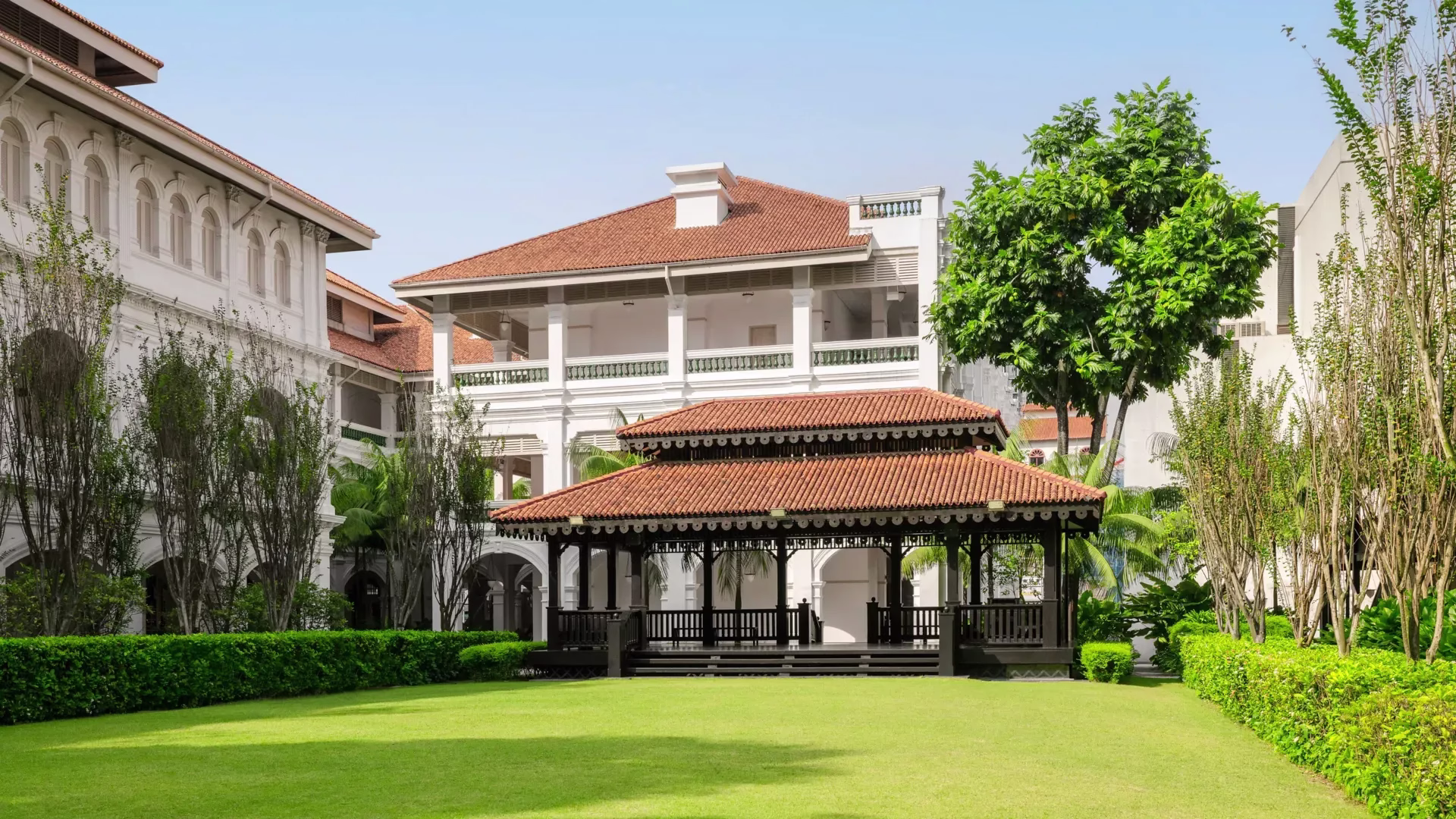 A beautifully landscaped hotel garden featuring a wooden event structure, surrounded by lush greenery and designed for outdoor gatherings on a sunny day.